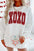 Valentine’s Day XOXO Glitter Round Neck Sweatshirt in white with red letters, held by a person holding a heart-patterned mug.