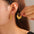 Gold-plated titanium steel leaf shape earrings worn by a person.