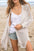 Openwork side slit open front long sleeve cardigan in beige acrylic, worn over casual summer outfit on beach.