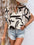 Perfee Printed Notched Half Sleeve Blouse with abstract design, styled with denim shorts.