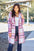 Full size plaid button up lapel collar coat with pockets in pink and white, worn by a woman outdoors.