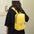 Solid color nylon backpack bag in yellow, medium size, worn by a person indoors.