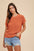 Annie Wear round neck short sleeve sweater in orange, styled with denim shorts.