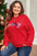 Plus size red sweater with "Merry" text, round neck, long sleeves, near Christmas tree.